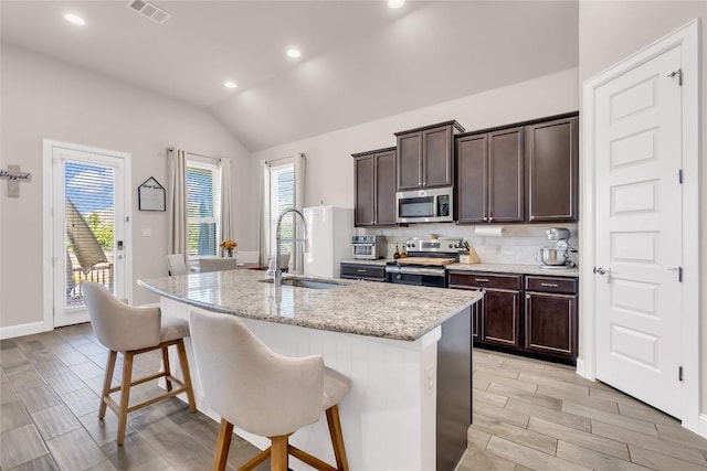 kitchen with a kitchen bar, sink, light stone counters, an island with sink, and stainless steel appliances