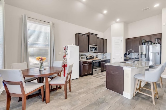 kitchen with sink, appliances with stainless steel finishes, a kitchen breakfast bar, light stone countertops, and an island with sink