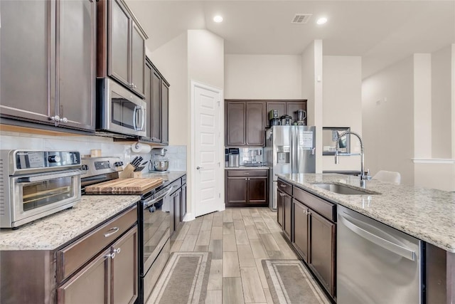 kitchen featuring sink, dark brown cabinets, stainless steel appliances, tasteful backsplash, and light stone counters