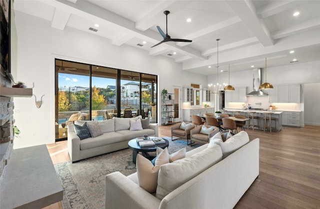 living room with a towering ceiling, wood-type flooring, a stone fireplace, and ceiling fan with notable chandelier