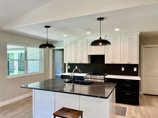 kitchen featuring stainless steel electric stove, sink, pendant lighting, and white cabinets