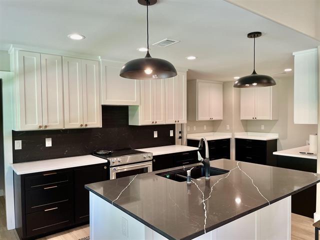 kitchen featuring sink, hanging light fixtures, a large island with sink, stainless steel range, and white cabinets