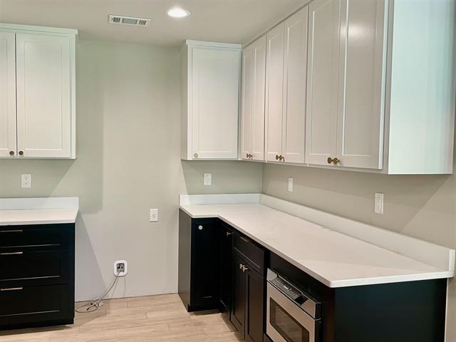 kitchen with white cabinetry, stainless steel microwave, and light wood-type flooring