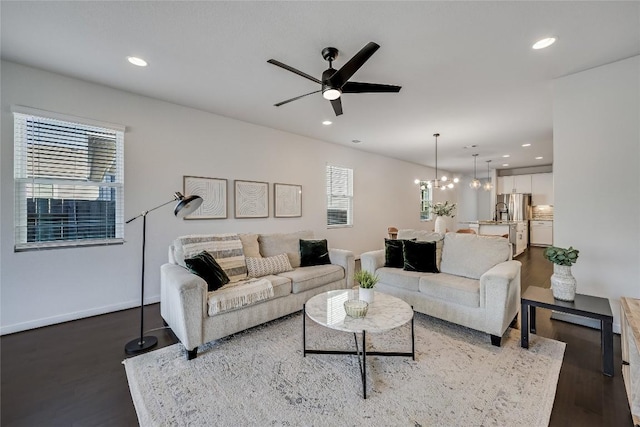 living room featuring dark wood-type flooring, ceiling fan with notable chandelier, and a wealth of natural light