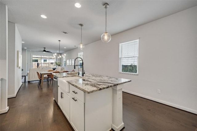 kitchen featuring light stone countertops, a center island with sink, white cabinets, and decorative light fixtures