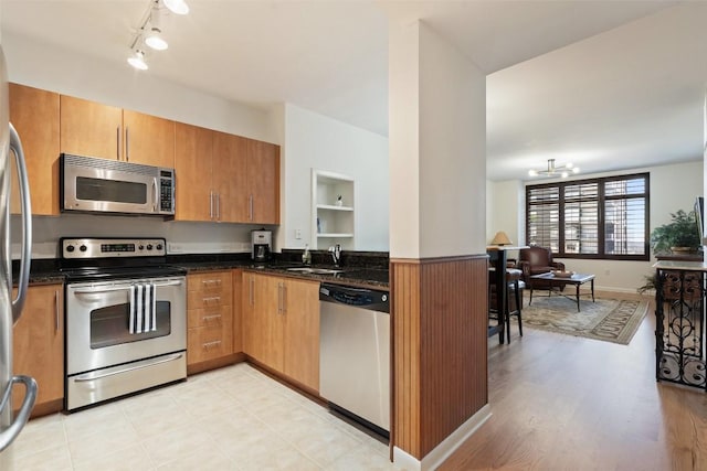 kitchen with sink, rail lighting, appliances with stainless steel finishes, an inviting chandelier, and dark stone counters