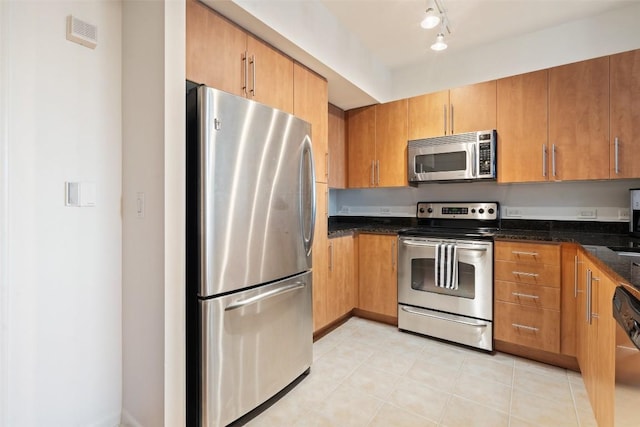 kitchen with rail lighting, light tile patterned flooring, appliances with stainless steel finishes, and dark stone counters