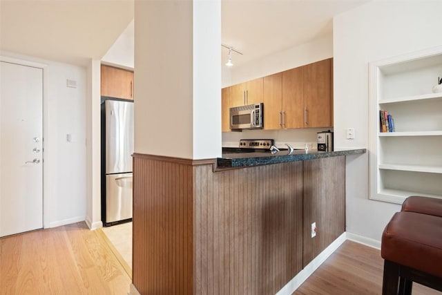 kitchen with built in features, rail lighting, kitchen peninsula, stainless steel appliances, and light hardwood / wood-style flooring