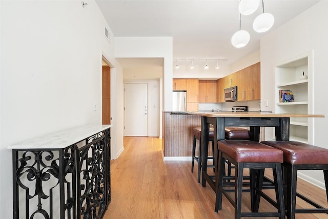 kitchen featuring a breakfast bar area, decorative light fixtures, light wood-type flooring, kitchen peninsula, and stainless steel appliances