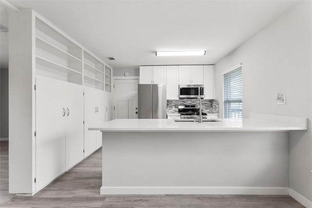 kitchen featuring white cabinetry, light wood-type flooring, appliances with stainless steel finishes, kitchen peninsula, and backsplash