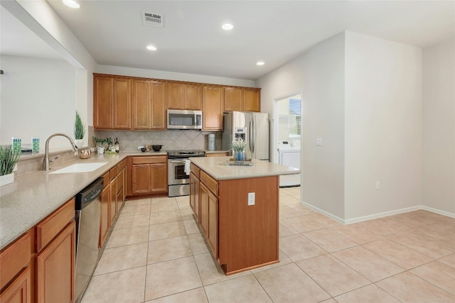 kitchen with washer / dryer, sink, light tile patterned floors, appliances with stainless steel finishes, and decorative backsplash