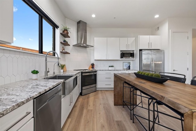 kitchen with sink, stainless steel appliances, light stone counters, white cabinets, and wall chimney exhaust hood