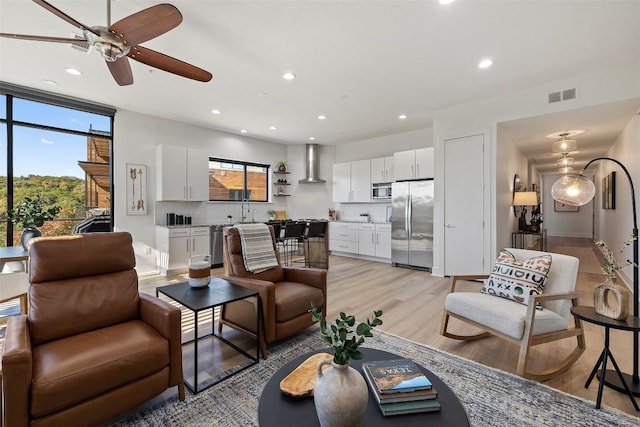 living room with sink, light hardwood / wood-style floors, and ceiling fan