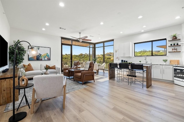 living room featuring ceiling fan, plenty of natural light, sink, and light wood-type flooring