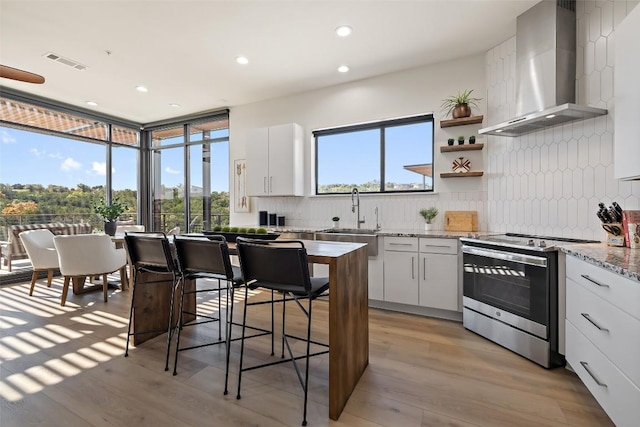 kitchen featuring stainless steel electric range oven, tasteful backsplash, white cabinetry, sink, and wall chimney range hood