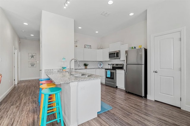 kitchen with a kitchen bar, sink, appliances with stainless steel finishes, kitchen peninsula, and white cabinets