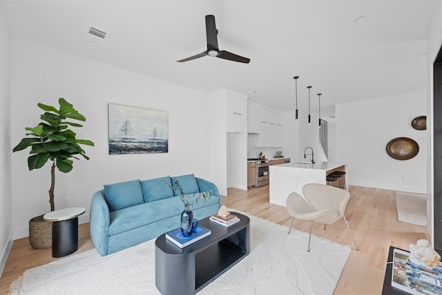 living room with sink, ceiling fan, and light wood-type flooring