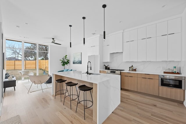 kitchen with sink, hanging light fixtures, a kitchen island with sink, decorative backsplash, and white cabinets