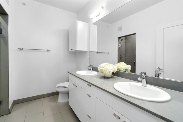 bathroom with tile patterned flooring, vanity, a tile shower, and toilet