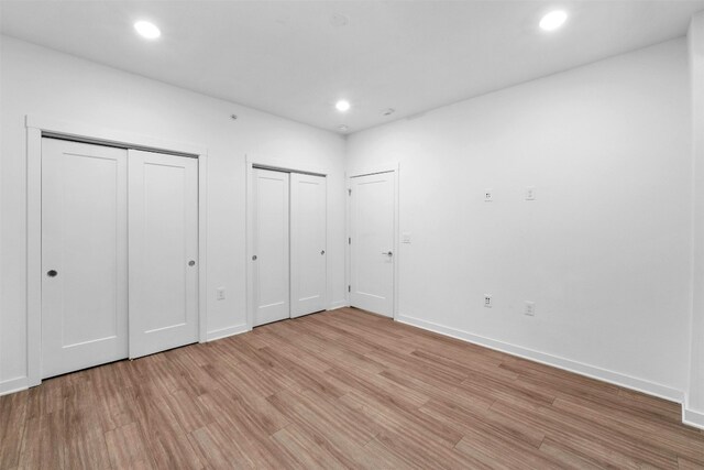 unfurnished bedroom featuring two closets and light hardwood / wood-style floors