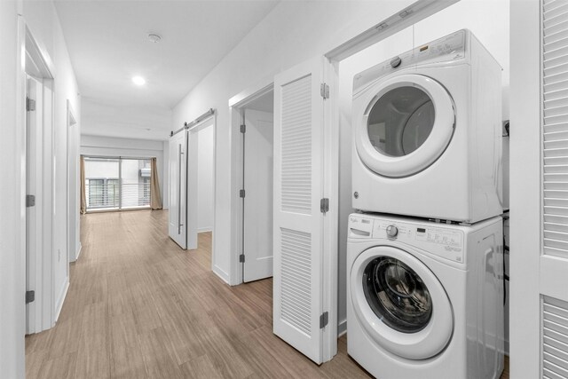 washroom with stacked washer and clothes dryer, a barn door, and light wood-type flooring