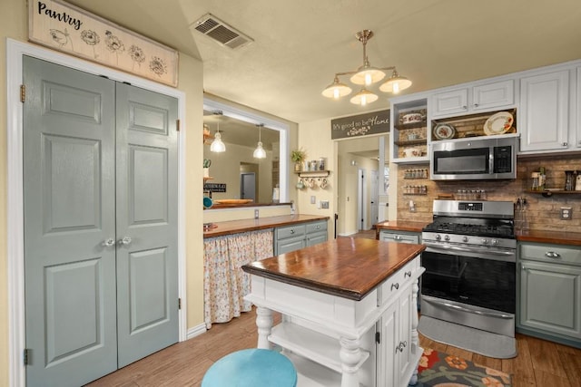 kitchen with pendant lighting, appliances with stainless steel finishes, butcher block counters, white cabinetry, and light wood-type flooring