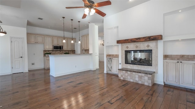 kitchen featuring dark wood-type flooring, a tile fireplace, ceiling fan, cream cabinets, and decorative light fixtures