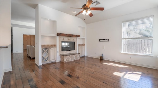 unfurnished living room featuring dark wood-type flooring, ceiling fan, a tiled fireplace, and vaulted ceiling