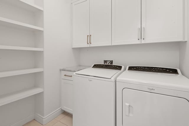 clothes washing area featuring washing machine and dryer, cabinets, and light tile patterned flooring