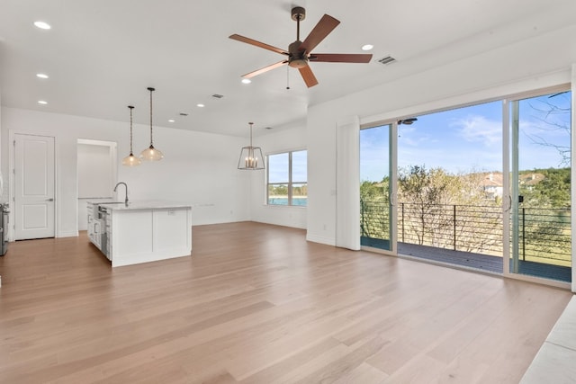 unfurnished living room featuring sink, ceiling fan with notable chandelier, and light wood-type flooring