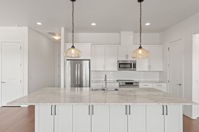 kitchen with appliances with stainless steel finishes, tasteful backsplash, wood-type flooring, white cabinets, and a center island with sink