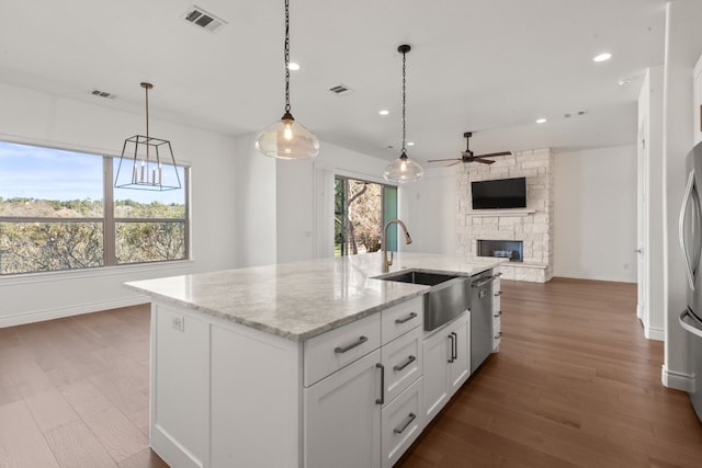 kitchen with a stone fireplace, white cabinetry, sink, a kitchen island with sink, and light stone countertops