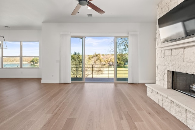 unfurnished living room with a water view, a healthy amount of sunlight, a fireplace, and light hardwood / wood-style floors