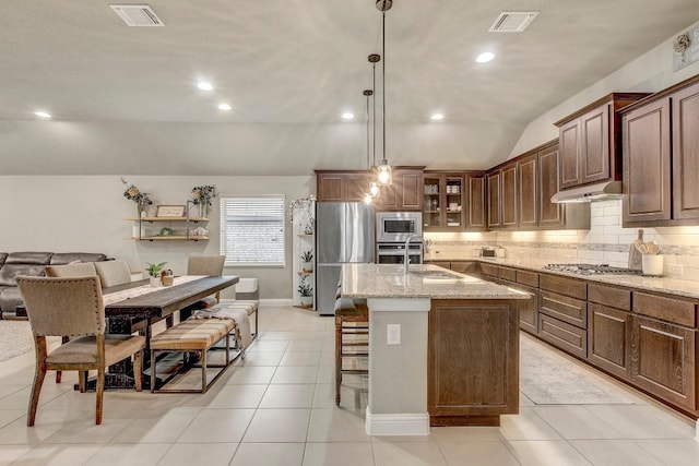 kitchen with pendant lighting, sink, appliances with stainless steel finishes, a kitchen island with sink, and light stone counters