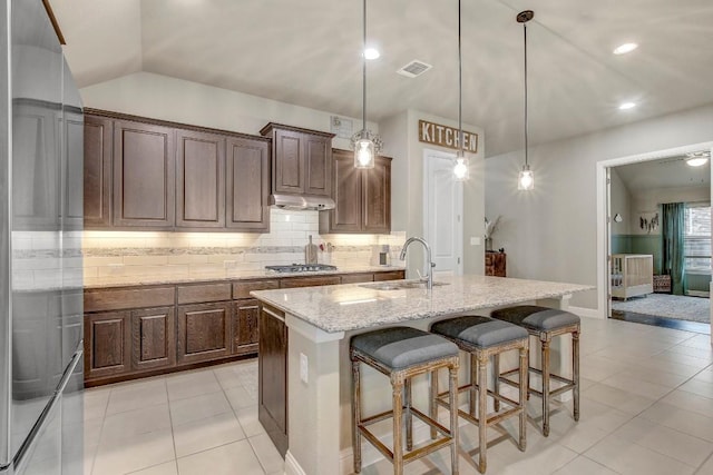 kitchen with sink, light stone counters, a center island with sink, appliances with stainless steel finishes, and pendant lighting