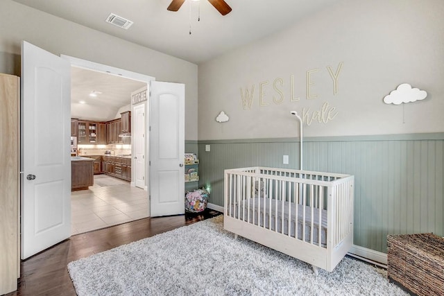 bedroom with wood-type flooring, a nursery area, and ceiling fan