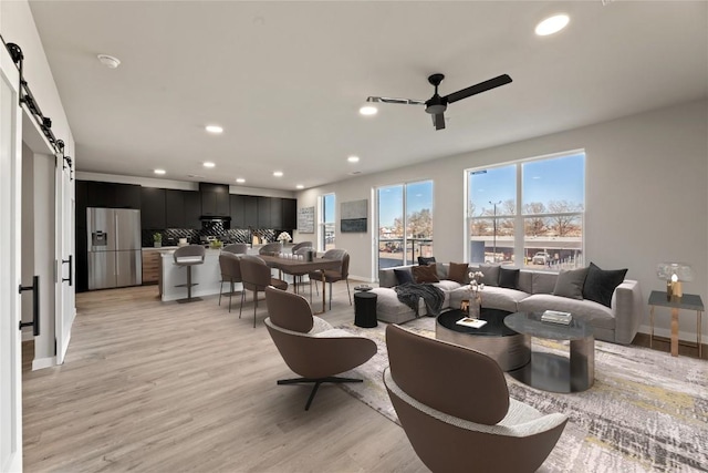 living room with light hardwood / wood-style floors, a barn door, and ceiling fan