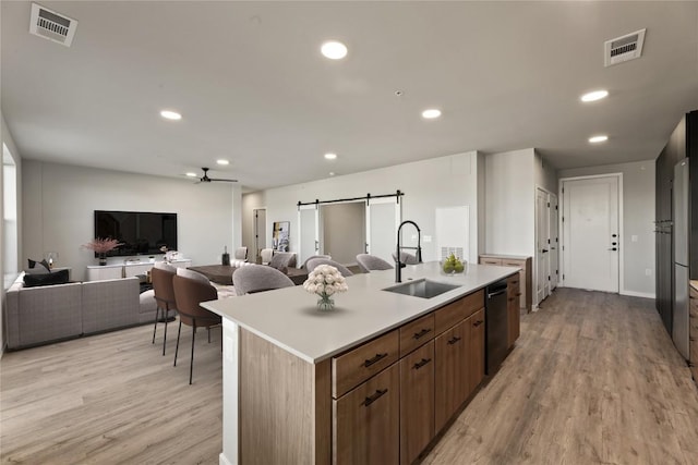 kitchen featuring sink, light wood-type flooring, dishwasher, a barn door, and a kitchen island with sink