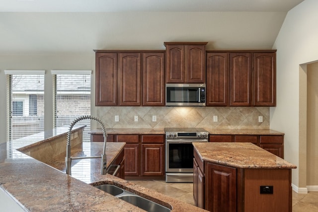 kitchen with light tile patterned floors, appliances with stainless steel finishes, backsplash, light stone countertops, and a kitchen island