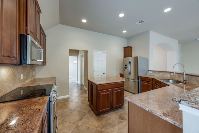 kitchen with appliances with stainless steel finishes, sink, backsplash, a center island, and light stone countertops