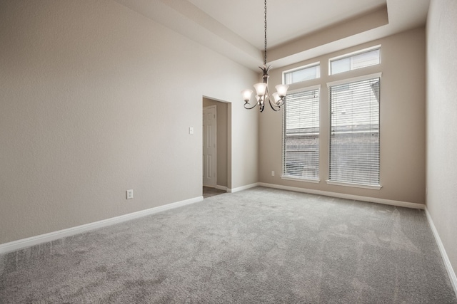 unfurnished room with a raised ceiling, carpet flooring, and a notable chandelier