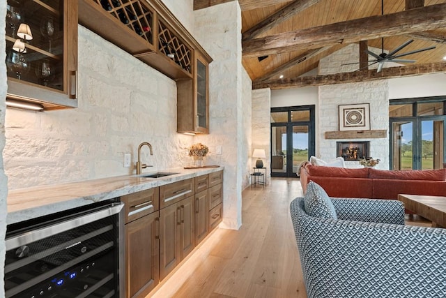 kitchen with a fireplace, beamed ceiling, sink, wine cooler, and light hardwood / wood-style floors