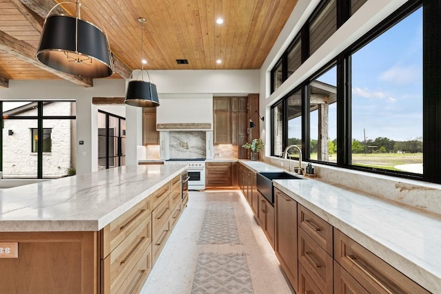 kitchen with a spacious island, sink, light stone counters, stainless steel range, and pendant lighting