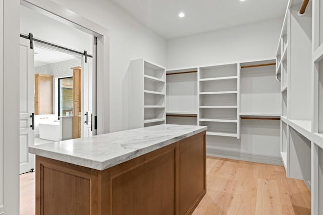 walk in closet with a barn door and light hardwood / wood-style floors