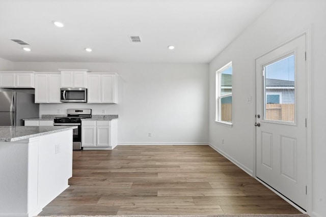 kitchen with white cabinetry, light stone counters, stainless steel appliances, and light wood-type flooring