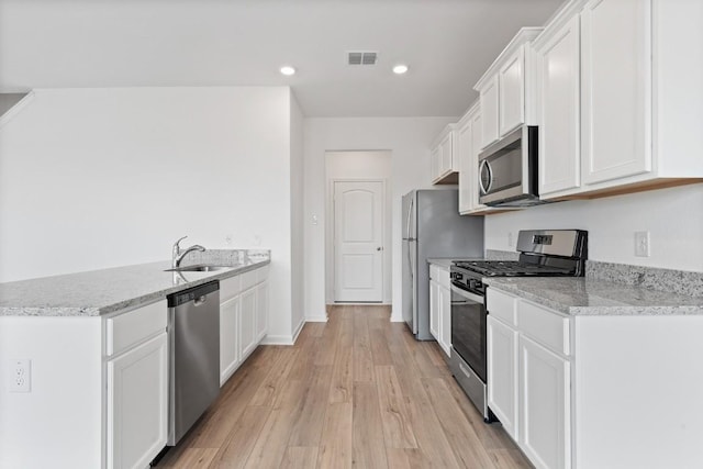 kitchen featuring stainless steel appliances, white cabinetry, light stone countertops, and sink