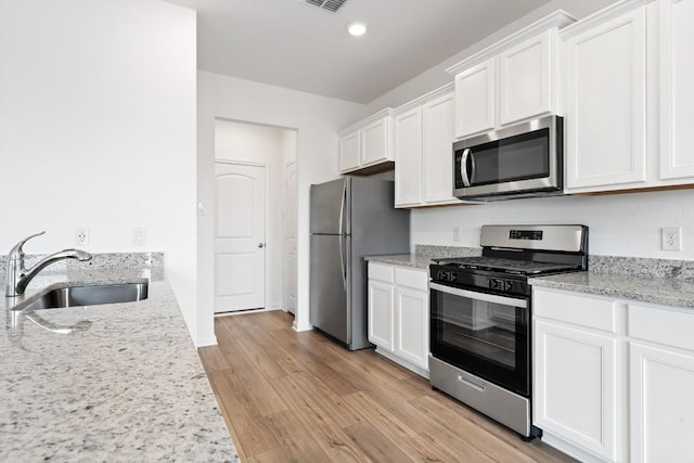 kitchen with sink, light stone counters, light wood-type flooring, appliances with stainless steel finishes, and white cabinets