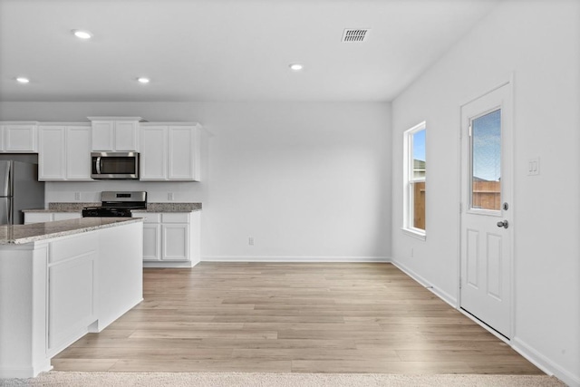 kitchen with stainless steel appliances, light stone countertops, white cabinets, and light hardwood / wood-style flooring