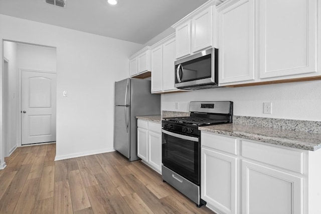 kitchen with light stone counters, light hardwood / wood-style flooring, white cabinets, and appliances with stainless steel finishes