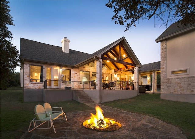 back house at dusk featuring a yard, a patio area, and an outdoor fire pit